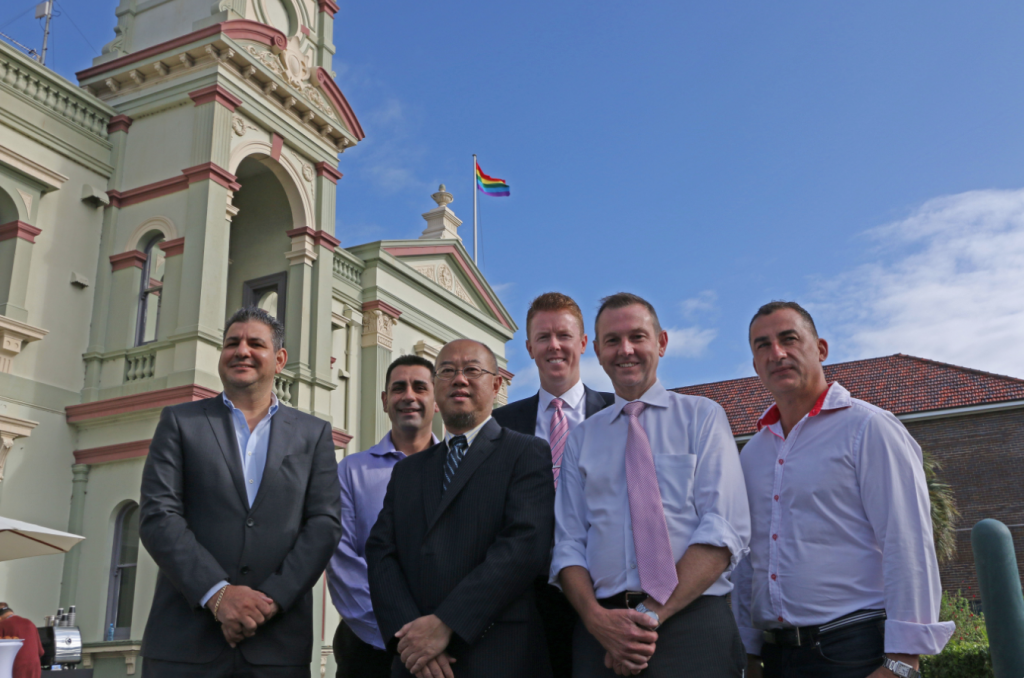 Randwick Deputy Mayor Anthony Andrews, Cr Harry Stavrinos, Mayor Ted Seng, Cr Scott Nash, Coogee state Liberal MP Bruce Notley-Smith and Mardi Gras CEO Michael Rolik with the rainbow flag outside Randwick Town Hall.